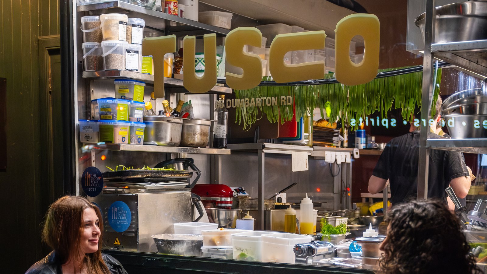 Tusco's kitchen pass and signage at 88 Dumbarton Road, with guests seated outside