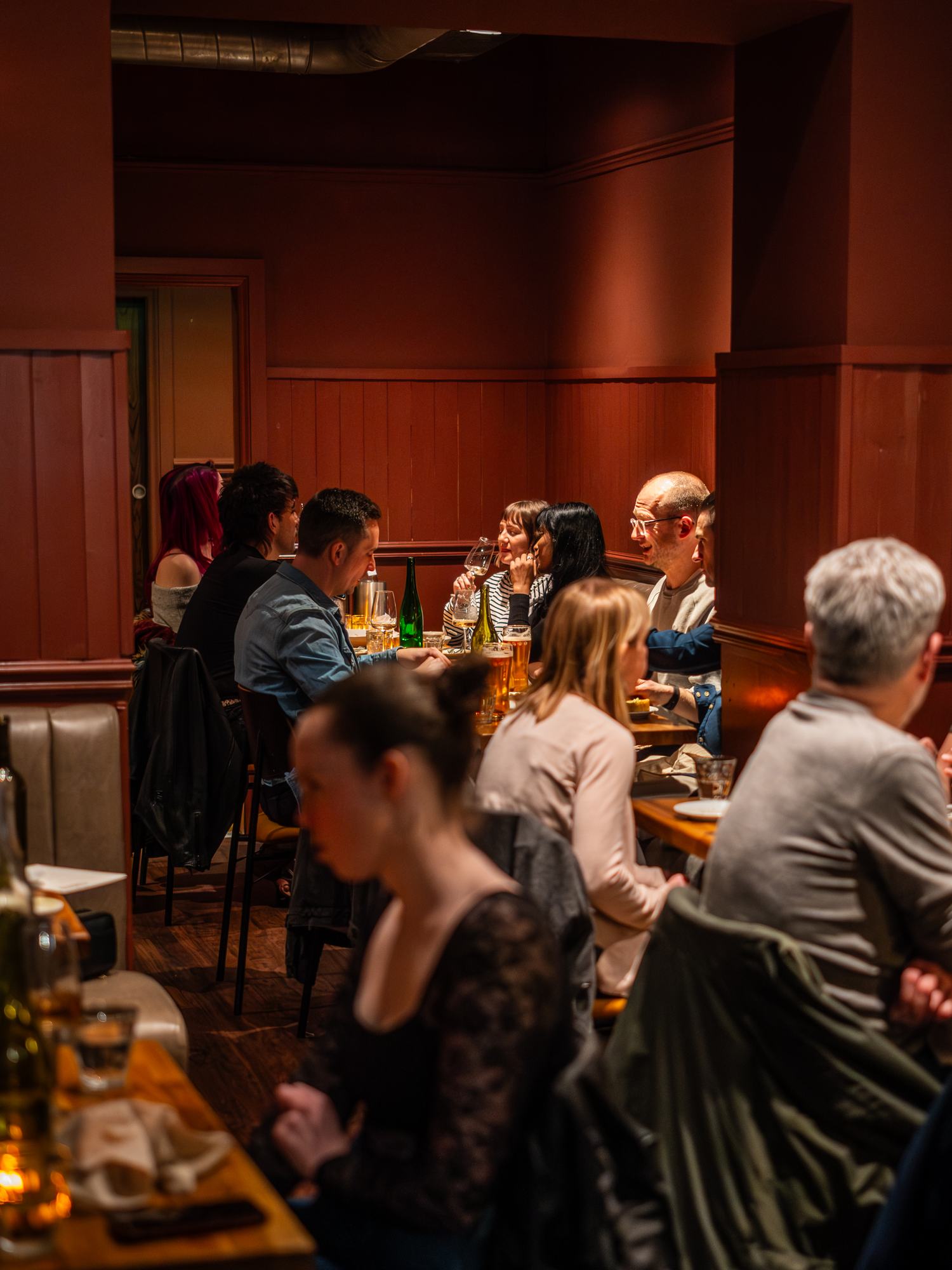 A busy evening in Tusco's dining room, diners at candlelit tables along the banquette and oxblood-panelled walls