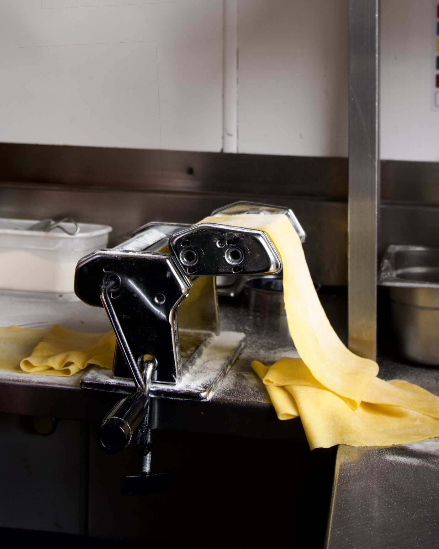 Fresh pasta sheet being hand-rolled through a pasta machine