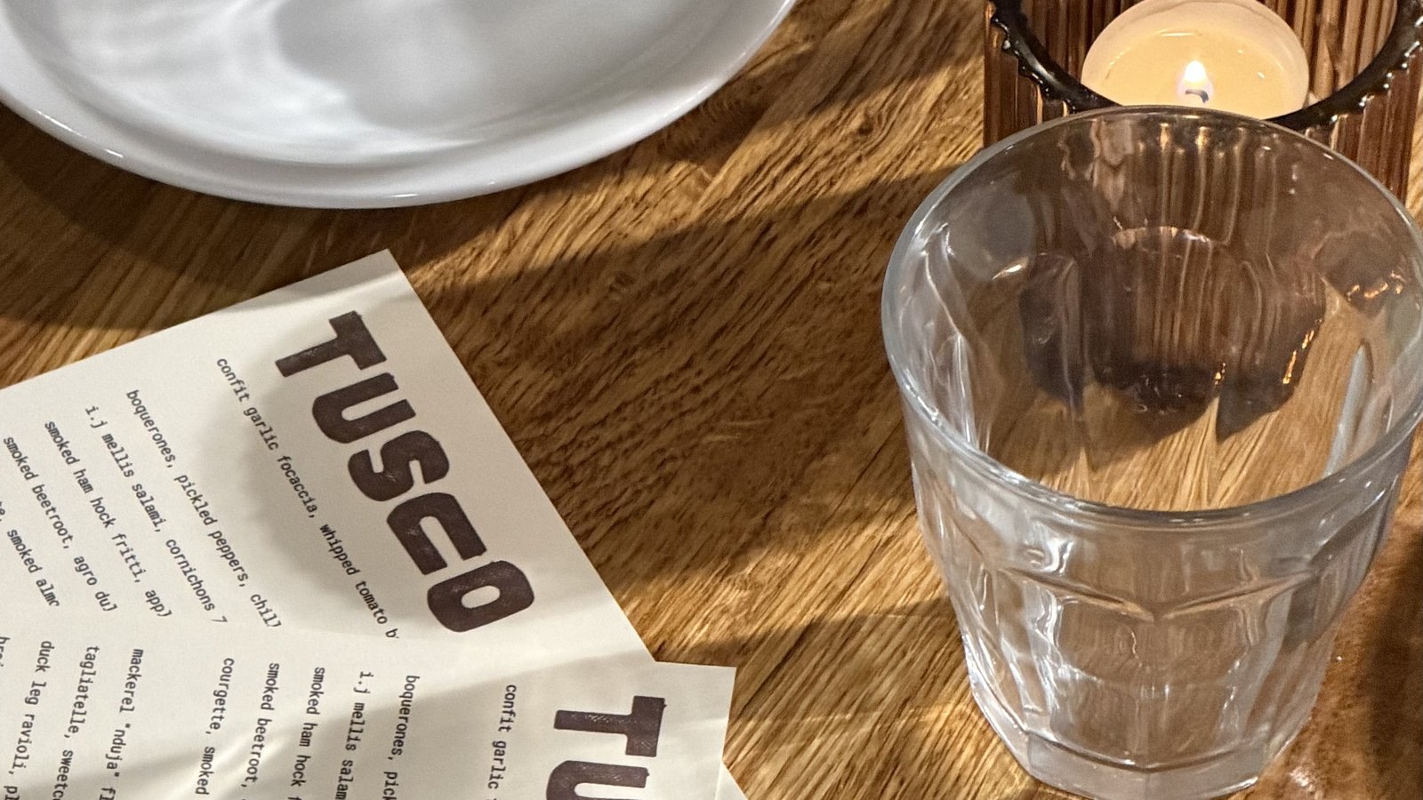 A table at Tusco set for the tasting menu, with a lit candle, wine glasses and the menu card